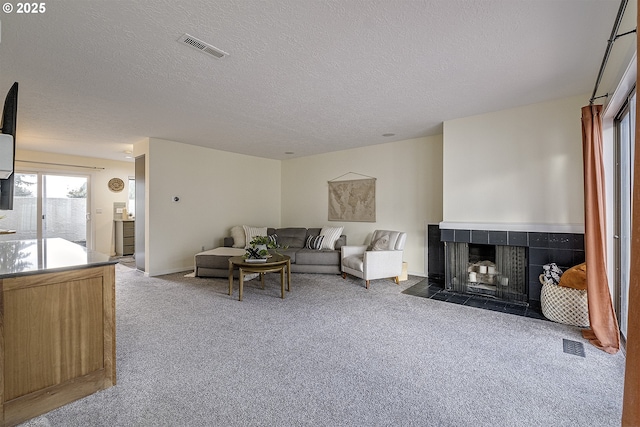 carpeted living room featuring a textured ceiling, visible vents, and a tiled fireplace