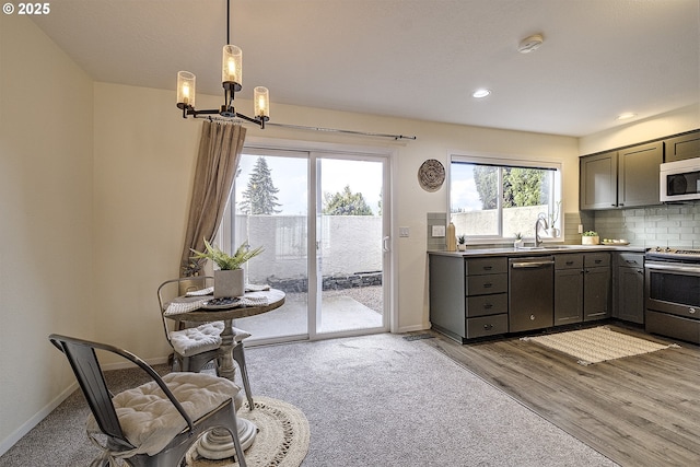 kitchen with hanging light fixtures, a sink, stainless steel appliances, light countertops, and backsplash