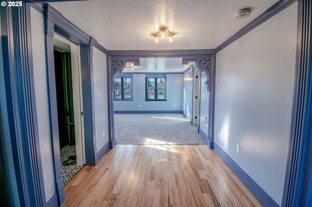 hallway with light hardwood / wood-style floors, a textured ceiling, and ornamental molding