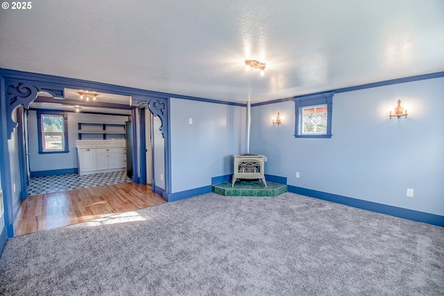 unfurnished living room featuring a wood stove, ornamental molding, carpet floors, and a textured ceiling