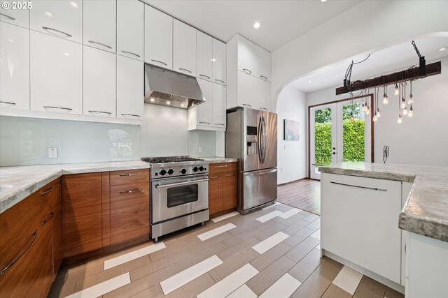 6035 NE 9th Ave, Portland, OR 97211 - kitchen featuring stainless steel appliances, under cabinet range hood, brown cabinetry, modern cabinets, and arched walkways