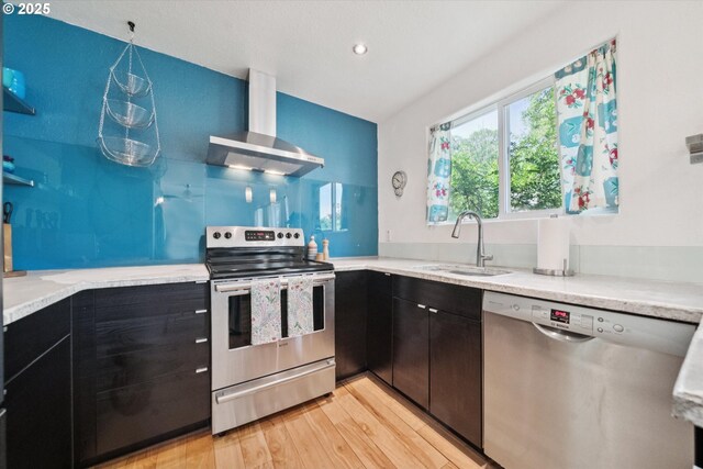 6035 NE 9th Ave, Portland, OR 97211 - kitchen with appliances with stainless steel finishes, wall chimney range hood, light wood finished floors, light stone countertops, and dark cabinetry
