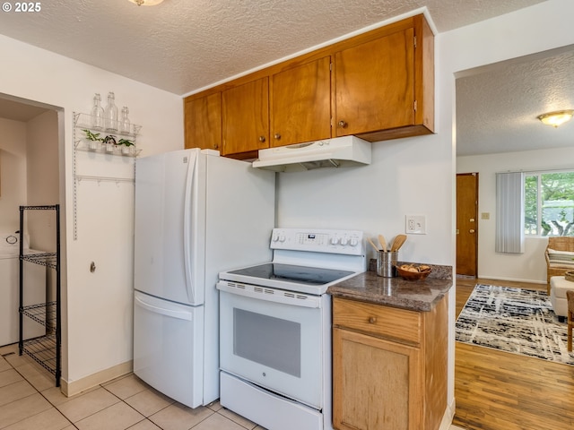 kitchen with white appliances, under cabinet range hood, a textured ceiling, dark countertops, and brown cabinetry