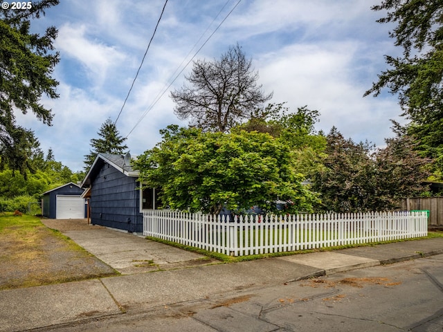 view of front facade with a detached garage, concrete driveway, a fenced front yard, and an outdoor structure