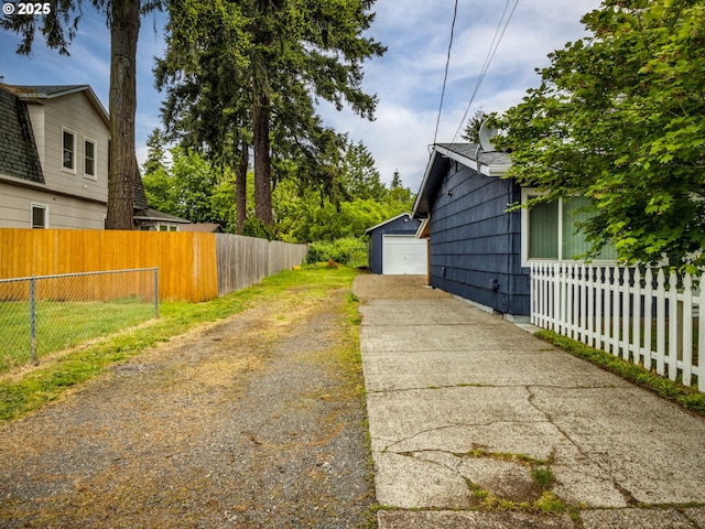 view of yard with driveway, fence, a detached garage, and an outbuilding