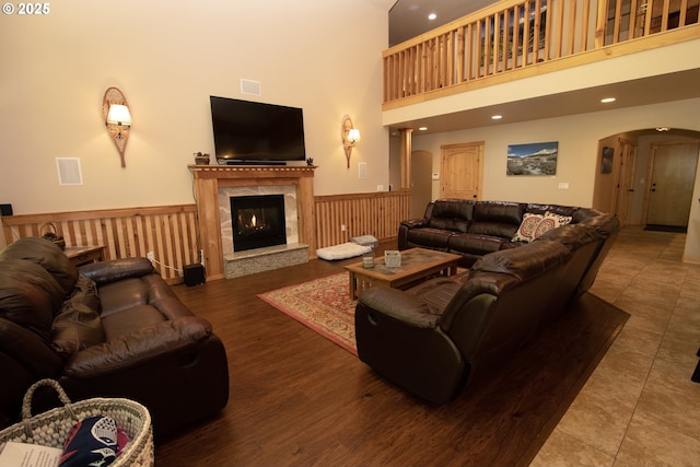 living room with visible vents, a towering ceiling, arched walkways, a fireplace, and a wainscoted wall