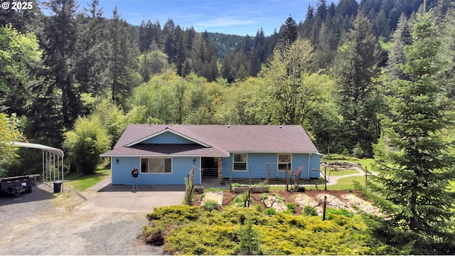 single story home featuring roof with shingles, driveway, and a forest view