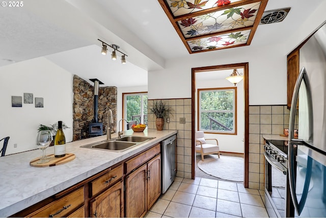kitchen featuring a wood stove, light countertops, a sink, light tile patterned floors, and stainless steel appliances