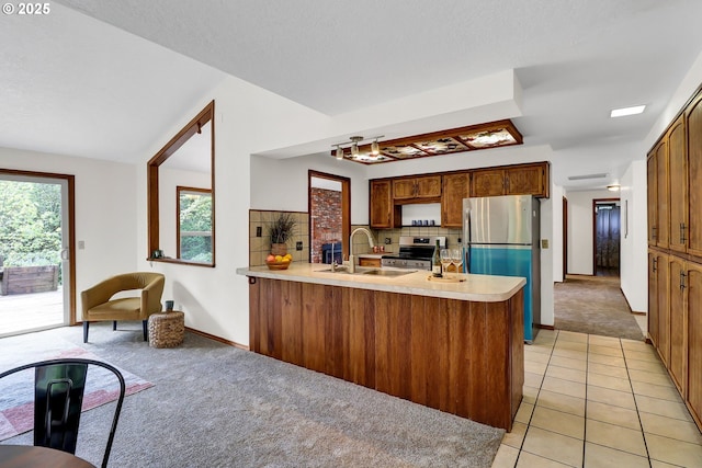 kitchen featuring a peninsula, light carpet, light countertops, a sink, and stainless steel appliances