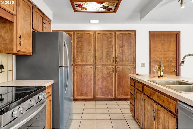 kitchen with a sink, light countertops, brown cabinetry, stainless steel appliances, and light tile patterned floors