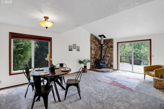 dining room with carpet floors, lofted ceiling, plenty of natural light, and a wood stove