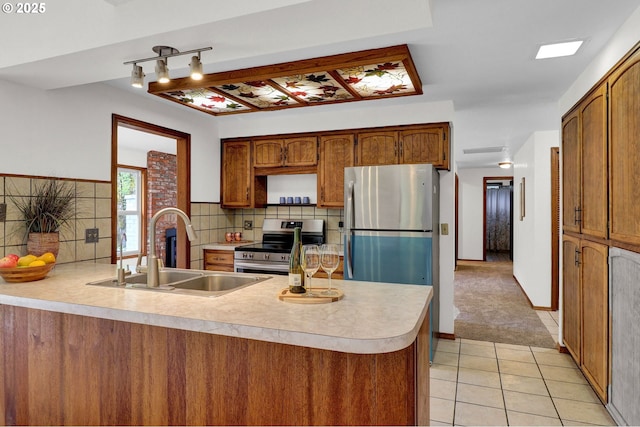 kitchen with a peninsula, light countertops, a sink, appliances with stainless steel finishes, and light tile patterned floors