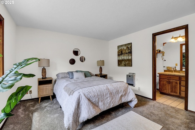 bedroom with light colored carpet, a sink, baseboards, and ensuite bath