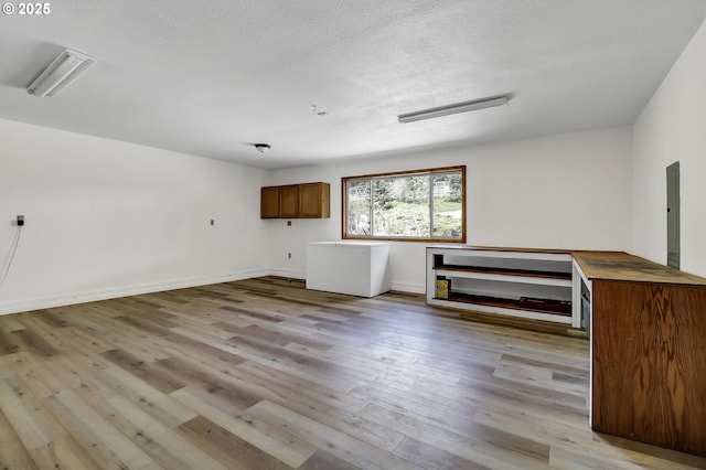 interior space featuring baseboards, a textured ceiling, wood finished floors, and electric panel