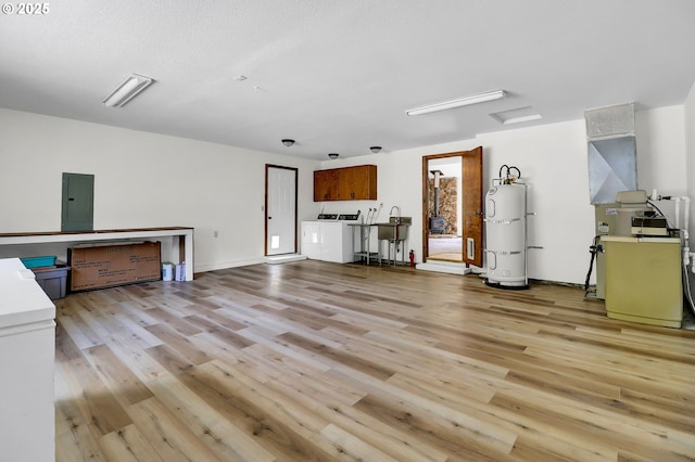 interior space with strapped water heater, washing machine and dryer, light wood finished floors, and electric panel