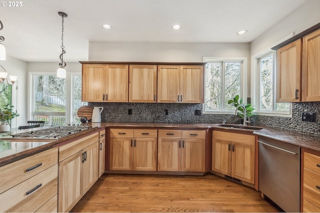 kitchen featuring decorative light fixtures, light wood finished floors, backsplash, appliances with stainless steel finishes, and a sink