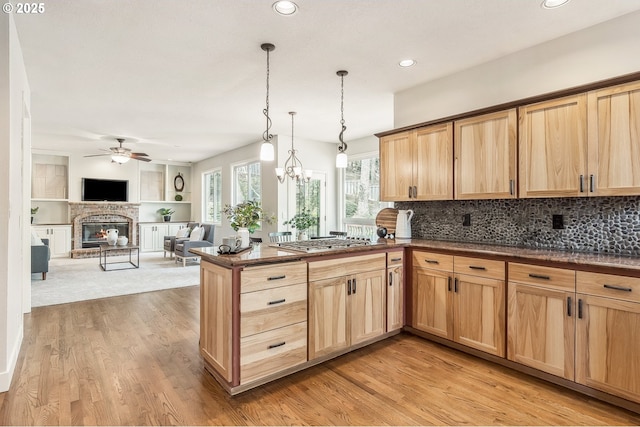 kitchen with stainless steel gas cooktop, a brick fireplace, light brown cabinets, light wood-type flooring, and a peninsula