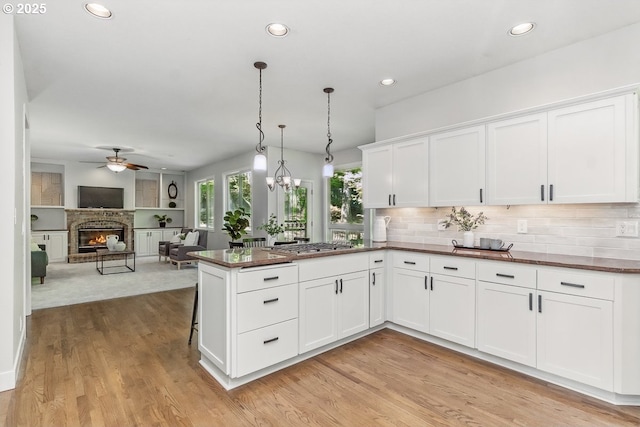 10915 SW Mourning Dove Pl, Beaverton, OR 97007 - kitchen with white cabinets, ceiling fan, a glass covered fireplace, light wood-style flooring, and stainless steel gas stovetop