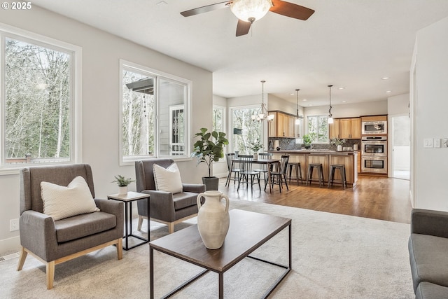 living room featuring recessed lighting, light wood-style flooring, baseboards, and ceiling fan with notable chandelier