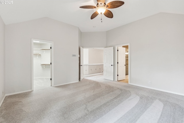 unfurnished bedroom featuring lofted ceiling, baseboards, a walk in closet, and light colored carpet