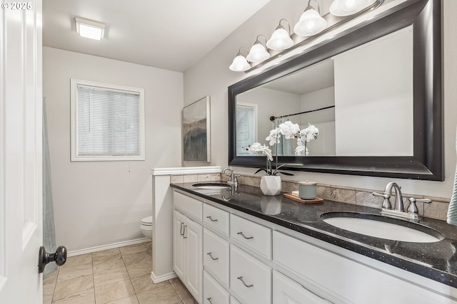 bathroom with toilet, double vanity, baseboards, and a sink