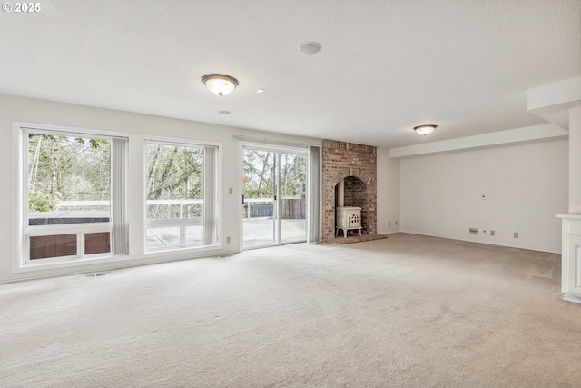 unfurnished living room with baseboards, visible vents, light colored carpet, a wood stove, and a textured ceiling