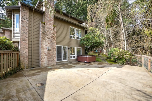 back of house with brick siding, a patio area, fence, and a hot tub