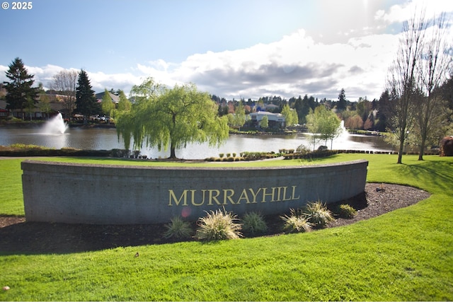 community sign with a water view and a lawn