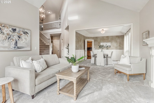 living area featuring a decorative wall, light carpet, a notable chandelier, stairs, and wainscoting