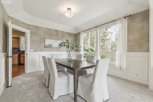 dining space featuring a decorative wall, wainscoting, and light colored carpet