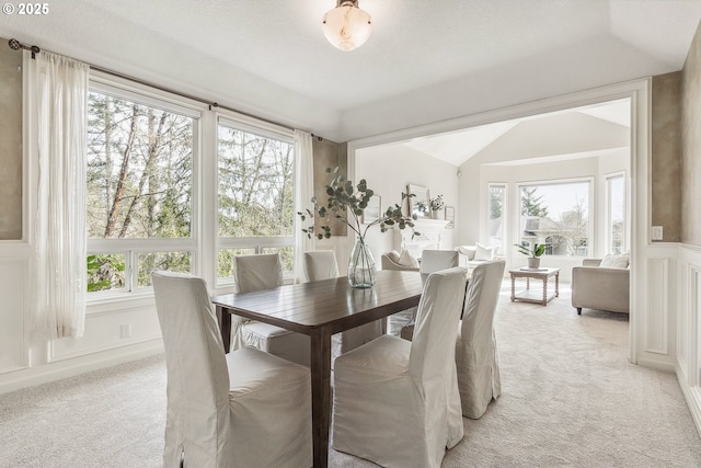 dining space featuring a wainscoted wall, vaulted ceiling, a decorative wall, and light colored carpet