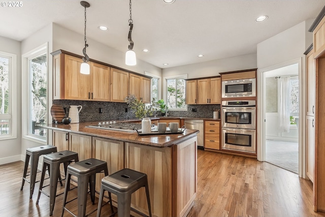 kitchen featuring appliances with stainless steel finishes, a peninsula, light wood finished floors, and tasteful backsplash