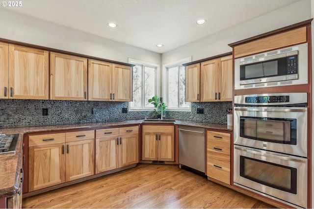 kitchen featuring light wood finished floors, tasteful backsplash, recessed lighting, appliances with stainless steel finishes, and a sink