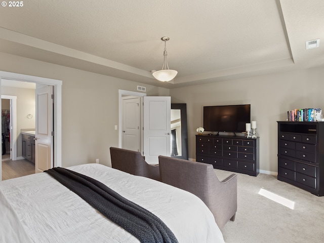 bedroom with baseboards, ensuite bathroom, visible vents, and a raised ceiling