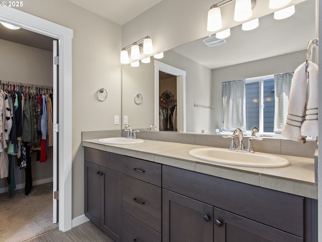 bathroom featuring a walk in closet, double vanity, baseboards, and a sink
