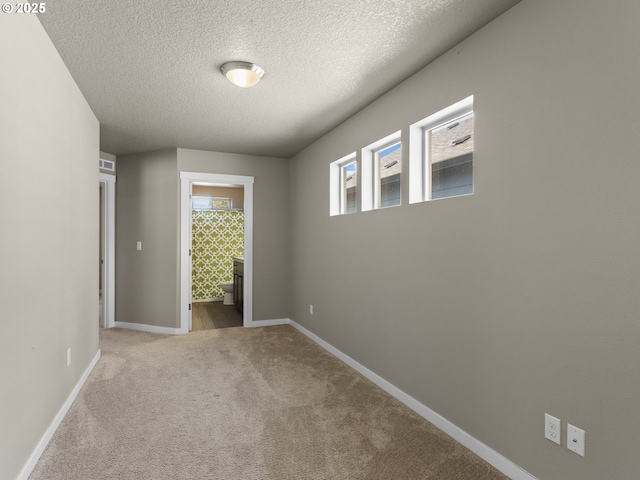 unfurnished room with a textured ceiling, carpet flooring, and baseboards