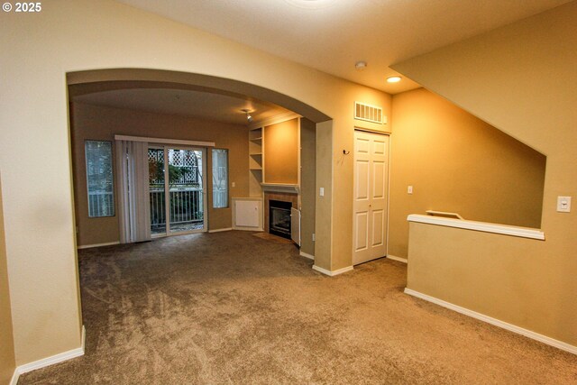 unfurnished living room featuring a tile fireplace, built in features, and carpet floors