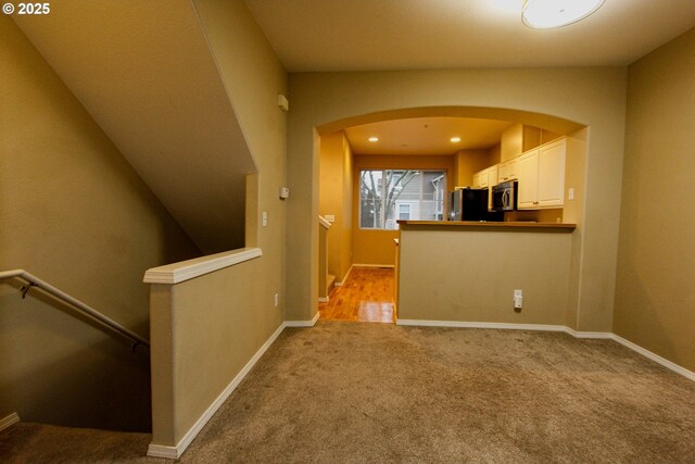 interior space with kitchen peninsula, light colored carpet, white cabinetry, and fridge