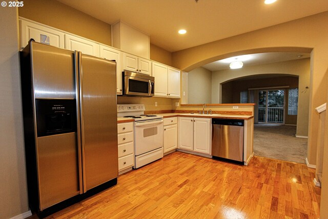 kitchen with sink, kitchen peninsula, light hardwood / wood-style floors, white cabinets, and appliances with stainless steel finishes