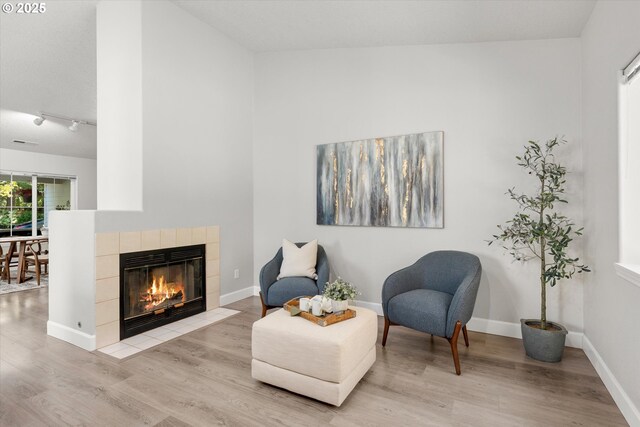 living area with light wood-style floors, a tiled fireplace, and baseboards