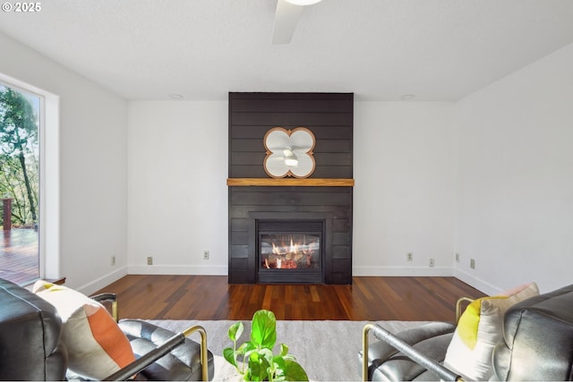 living room with a ceiling fan, a large fireplace, a textured ceiling, wood finished floors, and baseboards