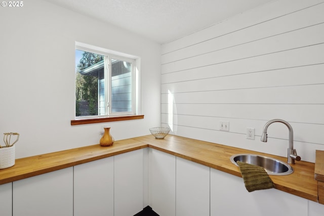 kitchen with butcher block countertops, white cabinets, and a sink