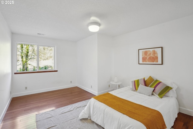 bedroom featuring a textured ceiling, baseboards, and hardwood / wood-style flooring