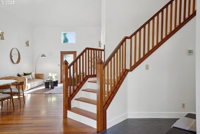 stairway with a towering ceiling, baseboards, and wood finished floors