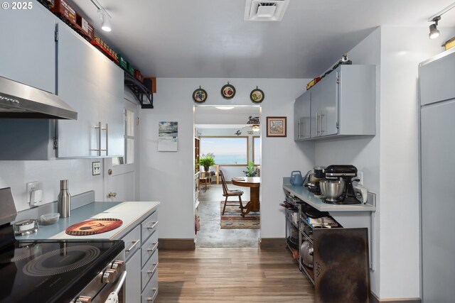 kitchen featuring rail lighting, dark wood-type flooring, exhaust hood, and stainless steel range with electric stovetop