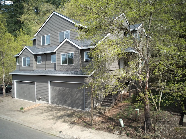 view of front of house with a garage, roof with shingles, a forest view, stairs, and driveway