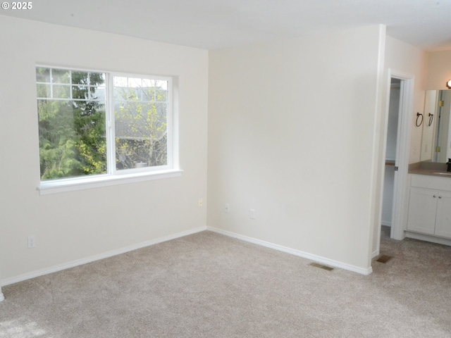 spare room with a healthy amount of sunlight, light colored carpet, baseboards, and visible vents