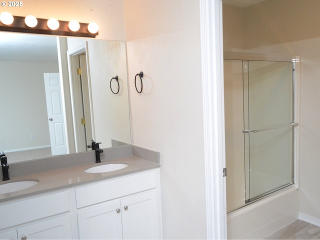 bathroom featuring combined bath / shower with glass door, double vanity, baseboards, and a sink