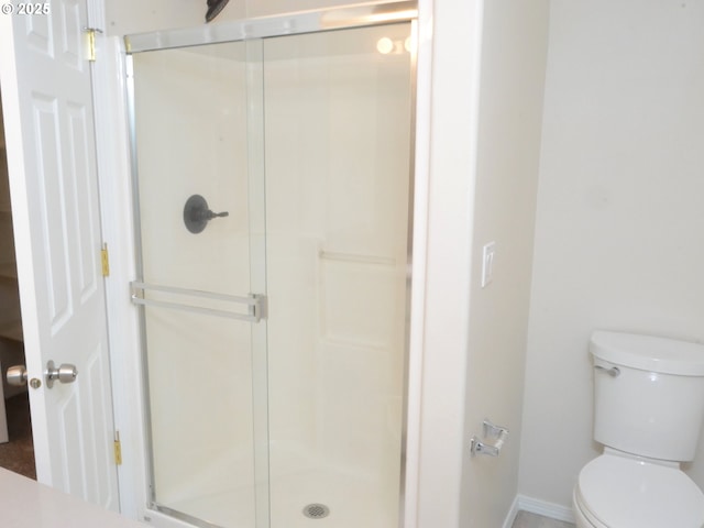 bathroom featuring toilet, a shower stall, and baseboards