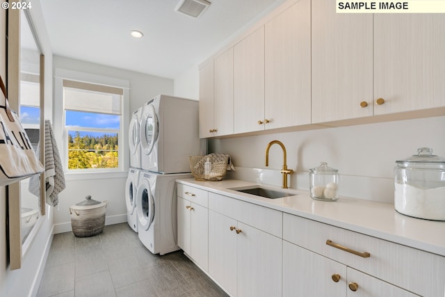 laundry area featuring visible vents, cabinet space, stacked washer / dryer, a sink, and baseboards